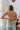 Back view of model wearing the Taking Chances Top, which features a blush colored ribbed material, a collar neck, a V neckline, a long sleeve, and a cropped fit.