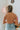 Back view of model wearing the Taking Chances Top, which features a blush colored ribbed material, a collar neck, a V neckline, a long sleeve, and a cropped fit.