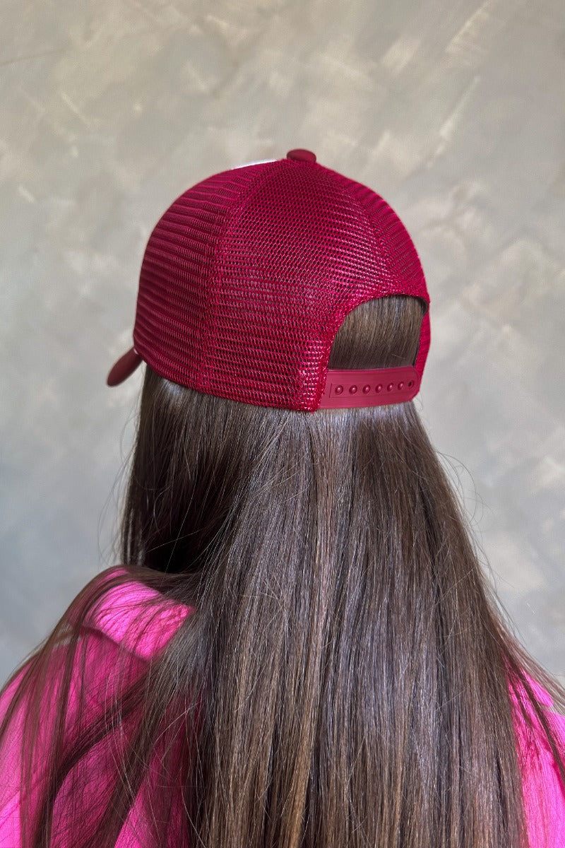 Back view of model wearing the Breast Cancer Gear: You Can Do It Trucker Hat that has a burgundy bill and back, a snapback, pink trim, and a cream front with an embroidered pink and burgundy graphic. 