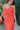Close front view of model wearing the All I've Ever Wanted Dress which features red orange fabric, midi length, ruffle details, a slit on the side, red orange lining, a v-neckline, adjustable spaghetti straps, and a monochromatic side zipper with a hook c