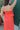 Close back view of model wearing the All I've Ever Wanted Dress which features red orange fabric, midi length, ruffle details, a slit on the side, red orange lining, a v-neckline, adjustable spaghetti straps, and a monochromatic side zipper with a hook cl
