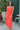 Front view of model wearing the All I've Ever Wanted Dress which features red orange fabric, midi length, ruffle details, a slit on the side, red orange lining, a v-neckline, adjustable spaghetti straps, and a monochromatic side zipper with a hook closure
