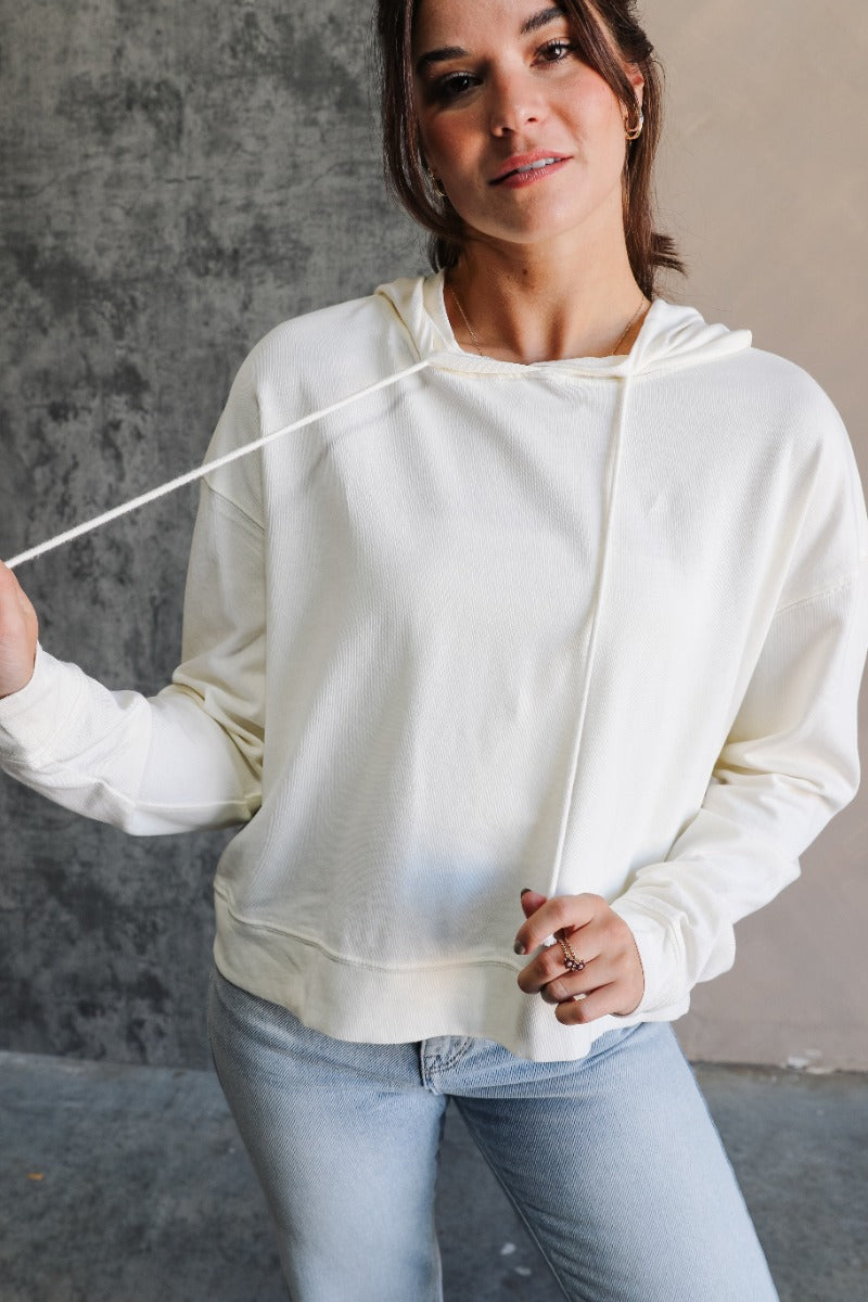 Front view of model wearing the Chloe Cream Hoodie Long Sleeve Sweatshirt which features cream cotton fabric, a thick hem, a high neckline with a hood attached and drawstring ties, a dropped shoulders, and long sleeves with cuffs.