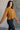 Side view of model wearing the Nicole Brown Cropped Long Sleeve Sweatshirt which features light brown cotton fabric, a cropped waist, a round neckline and long sleeves.