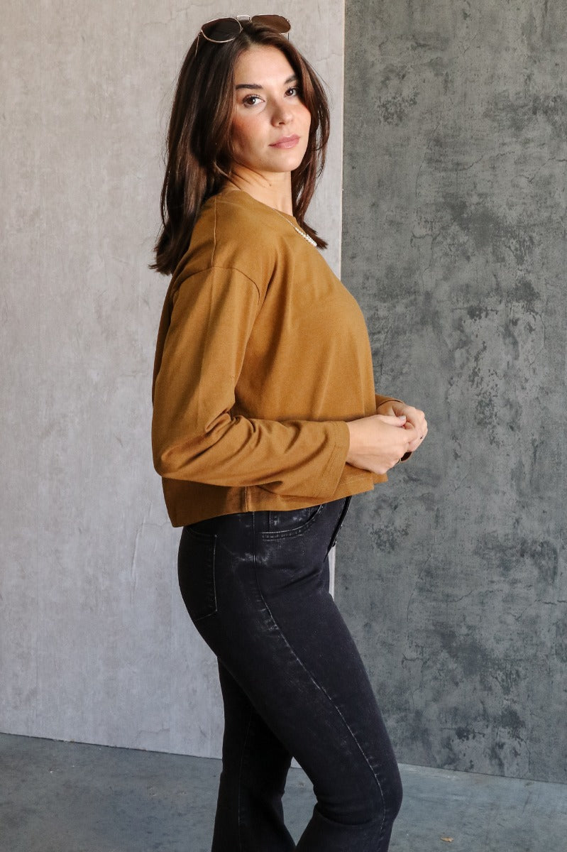 Side view of model wearing the Nicole Brown Cropped Long Sleeve Sweatshirt which features light brown cotton fabric, a cropped waist, a round neckline and long sleeves.
