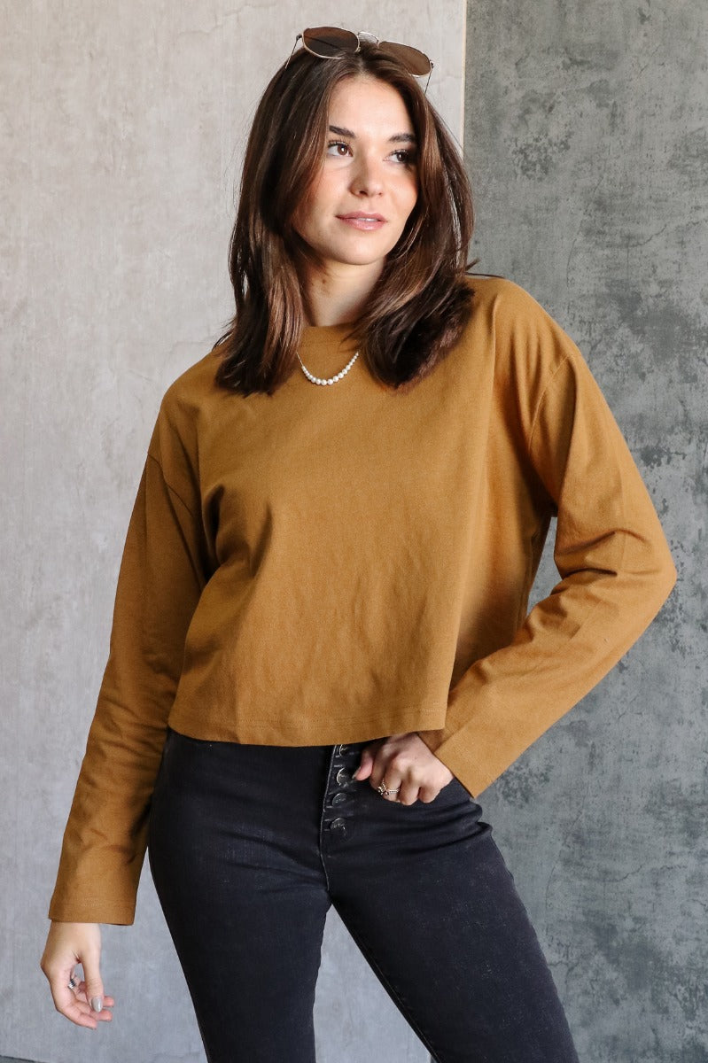 Front view of model wearing the Nicole Brown Cropped Long Sleeve Sweatshirt which features light brown cotton fabric, a cropped waist, a round neckline and long sleeves.