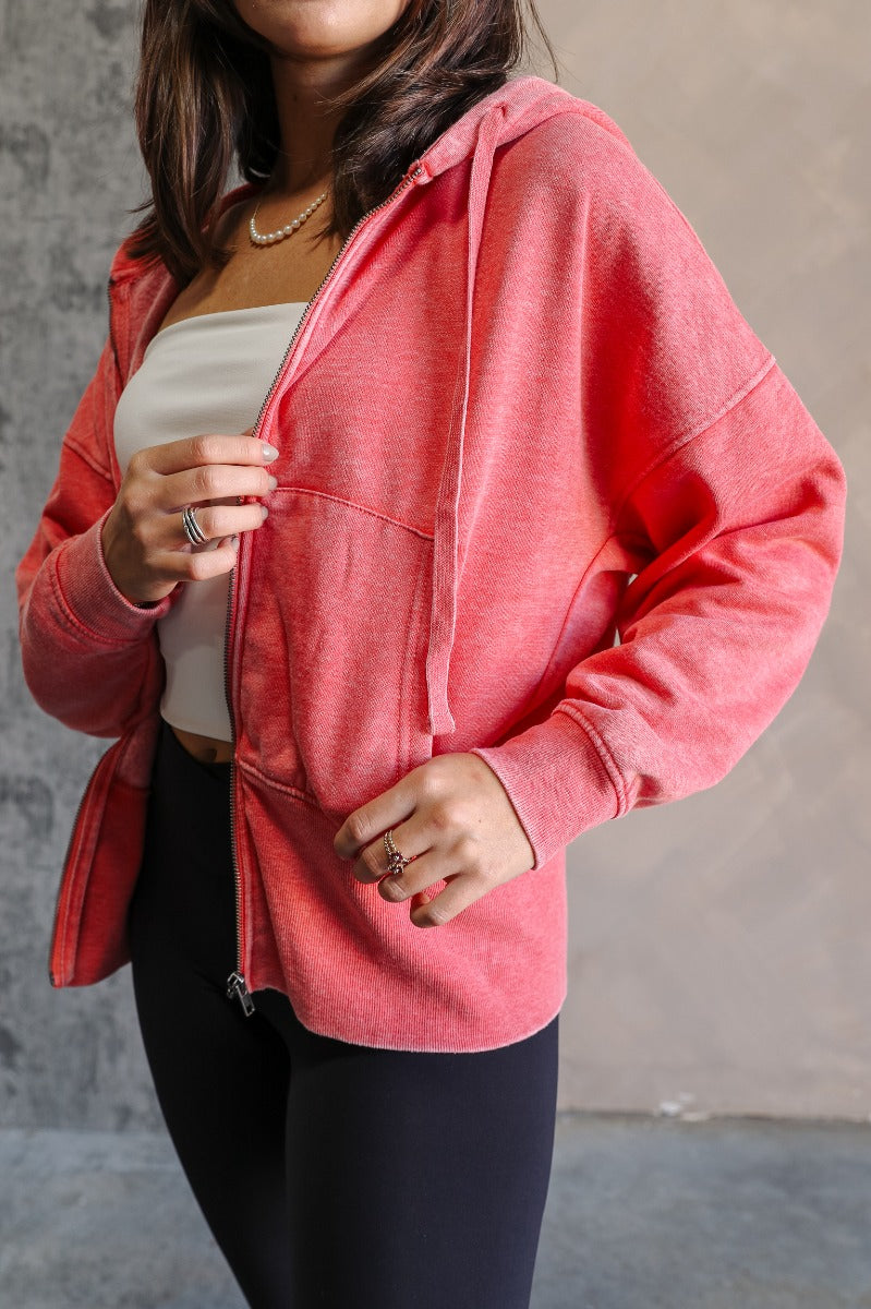 Front view of model wearing the Lauren Washed Red Zip-Up Hoodie Sweatshirt that has two pockets, a silver zipper, a hood with drawstrings, dropped shoulders, and long sleeves with cuffs.