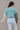 Back view of model wearing the Celeste Sage Multi Long Sleeve Sweater which features sage, light blue and cream cable knit fabric, a colorblock pattern, a cropped waist, ribbed trim, a round neckline, dropped shoulders, and long balloon sleeves with cuffs