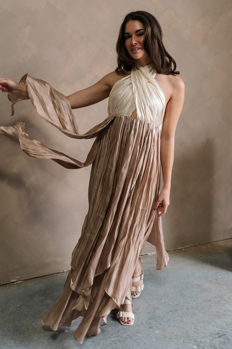Full body front view of model wearing the Rosalia Cream & Taupe Layered Satin Midi Dress that has cream and taupe satin, midi length, layered pleated details, a halter neck and open back.