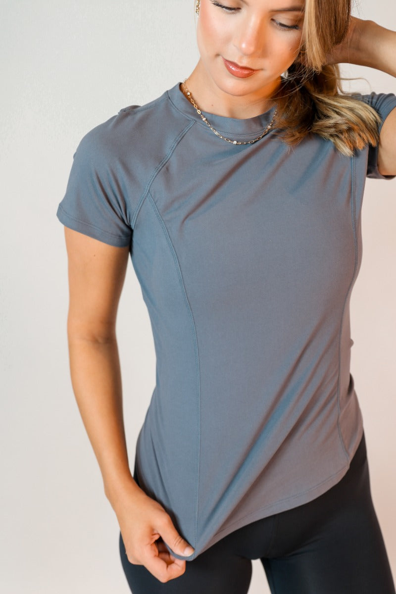 Close up view of model wearing the Robin Grey Athletic Short Sleeve Top which features grey athleisure fabric, monochrome stitch details, a scooped neckline, and short sleeves.