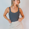 Front view of model wearing the Avery Charcoal Grey Sleeveless Bodysuit which features charcoal grey knit fabric, a scooped neckline, thick straps, and a thong bottom with snap closures.