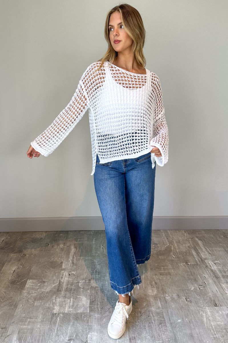 Full body view of model wearing the Sahara Ivory Crochet Knit Long Sleeve Sweater which features ivory open knit fabric, a high-low hem, slits on each side, a round neckline and long flare sleeves.