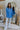 Full body front view of model wearing the Ocean Eyes Button-Up Top that has blue fabric, a high-low hem, an oversized fit, a button-up front with a collar, front chest pockets, and long sleeves.