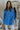 Front view of model wearing the Ocean Eyes Button-Up Top that has blue fabric, a high-low hem, an oversized fit, a button-up front with a collar, front chest pockets, and long sleeves.