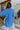 Back view of model wearing the Ocean Eyes Button-Up Top that has blue fabric, a high-low hem, an oversized fit, a button-up front with a collar, front chest pockets, and long sleeves.