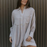 Front view of model wearing the On Cloud Nine Dress that has light grey fabric, a mini-length hem, front chest pockets, a button-up front, side pockets, a collar, and long sleeves.