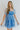 Front view of model wearing the Forget Me Not Babydoll Dress that has blue and light blue organza fabric with a floral pattern, a mini-length hem, a square neck, a back zipper with a hook closure, and short puff sleeves