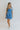 Full body front view of model wearing the Forget Me Not Babydoll Dress that has blue and light blue organza fabric with a floral pattern, a mini-length hem, a square neck, a back zipper with a hook closure, and short puff sleeves