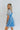 Side view of model wearing the Forget Me Not Babydoll Dress that has blue and light blue organza fabric with a floral pattern, a mini-length hem, a square neck, a back zipper with a hook closure, and short puff sleeves