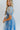 Side view of model wearing the Forget Me Not Babydoll Dress that has blue and light blue organza fabric with a floral pattern, a mini-length hem, a square neck, a back zipper with a hook closure, and short puff sleeves