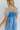 Close back view of model wearing the Forget Me Not Babydoll Dress that has blue and light blue organza fabric with a floral pattern, a mini-length hem, a square neck, a back zipper with a hook closure, and short puff sleeves