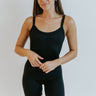 Front view of model wearing the Can You Keep Up Bodysuit that features black stretch fabric, a round neckline, adjustable thick straps, and fitted shorts.