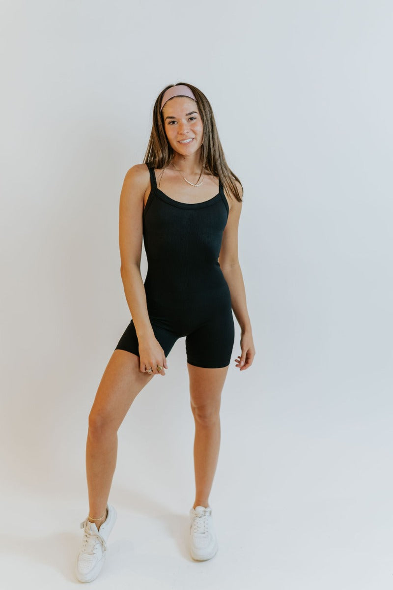 Full body front view of model wearing the Can You Keep Up Bodysuit that features black stretch fabric, a round neckline, adjustable thick straps, and fitted shorts.