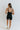 Full body back view of model wearing the Can You Keep Up Bodysuit that features black stretch fabric, a round neckline, adjustable thick straps, and fitted shorts.