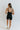 Full body back view of model wearing the Can You Keep Up Bodysuit that features black stretch fabric, a round neckline, adjustable thick straps, and fitted shorts.