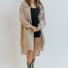 Front view of model wearing the It's Fate Shirt Dress that has taupe fabric, a button-up front, a collar, chest pockets, a midi-length high-low hem with slits, and drop-shoulder long sleeves. Worn unbuttoned over romper.