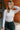 Front view of model wearing the Piper White Knit Long Sleeve Bodysuit which features white knit fabric, high neckline, long sleeves and thong bottom with button snap closures.