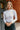 Front view of model wearing the Piper White Knit Long Sleeve Bodysuit which features white knit fabric, high neckline, long sleeves and thong bottom with button snap closures.