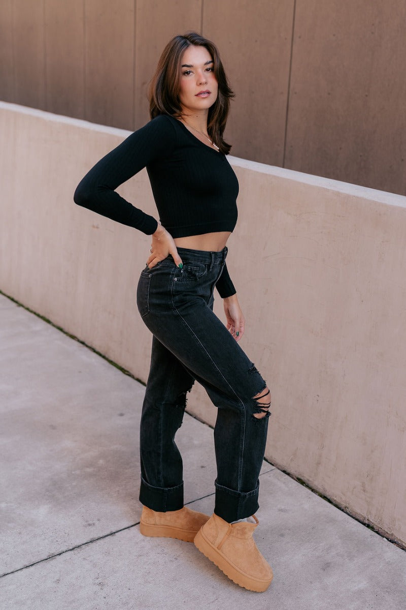 Full body side view of model wearing the Judy Blue: Alicia Black Straight Leg Jeans which features washed black denim, two front pockets, two back pockets, front zipper with button closure, belt loops, distressed details, busted knee details and straight 