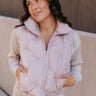 Front view of model wearing the Adelaide Light Rose Puffer Vest that has pale pink puffer fabric with tufted details, a zip-up front with a high neck, drawstrings at the waist, and front slit pockets.