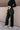 Side view of model wearing the Alexis Black Faux Leather Pants which features black faux leather, front zipper with button closure, two front pockets, two back pockets, belt loops and wide pant legs.