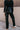 Back view of model wearing the Alexis Black Faux Leather Pants which features black faux leather, front zipper with button closure, two front pockets, two back pockets, belt loops and wide pant legs.