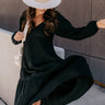 Full body view of model wearing the Wrenley Black Long Sleeve Midi Dress which features black gauze fabric, a tiered body, midi-length hem, long balloon sleeves with elastic trim, side pockets, a v neckline, and a smocked back.