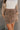 Front view of model wearing the Journey Mocha Brown Cargo Mini Skirt which features taupe brown textured soft fabric, two fornt cargo pocket with zipper closure, elastic waistband with tie and mini length.