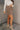 Full body side view of model wearing the Journey Mocha Brown Cargo Mini Skirt which features taupe brown textured soft fabric, two fornt cargo pocket with zipper closure, elastic waistband with tie and mini length.