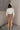 Full body back view of model wearing the Journey Mocha Brown Cargo Mini Skirt which features taupe brown textured soft fabric, two fornt cargo pocket with zipper closure, elastic waistband with tie and mini length.