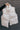 Front view of model holding the Winnie Iridescent White Puffer Vest that has a zip-up front with a high neck, front pockets, and adjustable drawstrings.
