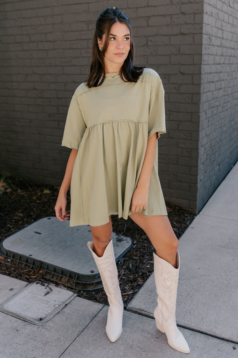 Full body view of model wearing the Leah Light Olive Short Sleeve Mini Dress which features light olive knit fabric, oversized peplum body, raw hem details, round neckline and short sleeves.