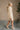 full body side view of model wearing the Isabella Cream Turtleneck Sweater Dress that has cream cable knit fabric, ribbed trim, mini length, a turtleneck, dropped shoulders, and long balloon sleeves with ribbed cuffs.