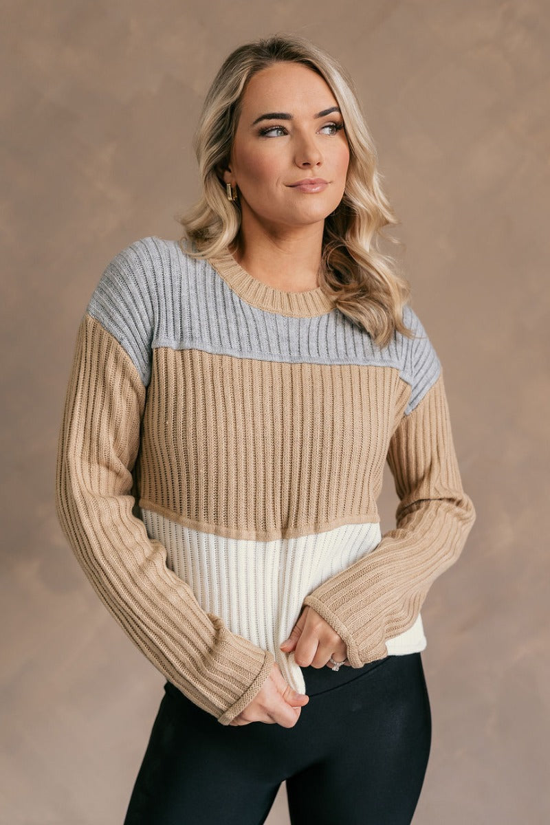 Front view of model wearing the Rylee Taupe Multi Striped Long Sleeve Sweater which features taupe, white and grey ribbed knit fabric, color block pattern, round neckline and long sleeves.