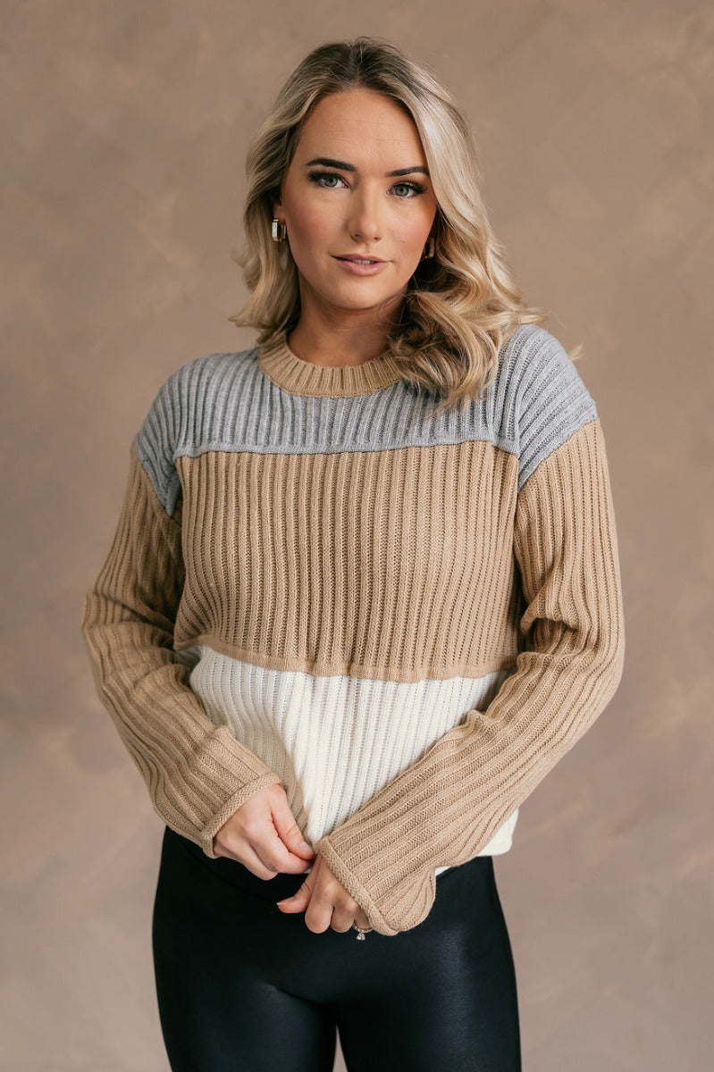 Front view of model wearing the Rylee Taupe Multi Striped Long Sleeve Sweater which features taupe, white and grey ribbed knit fabric, color block pattern, round neckline and long sleeves.