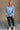 Full body view of model wearing the Sadie Light Blue Long Sleeve Sweatshirt which features light blue knit fabric, distressed details, ribbed hem, slits on each side, round neckline, dropped shoulders and long balloon sleeves with cuffs.