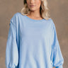 Front view of model wearing the Sadie Light Blue Long Sleeve Sweatshirt which features light blue knit fabric, distressed details, ribbed hem, slits on each side, round neckline, dropped shoulders and long balloon sleeves with cuffs.