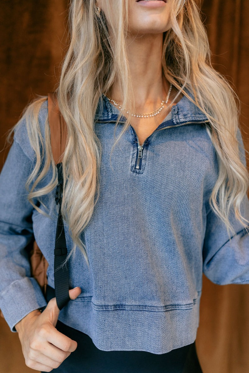 Detail view of model wearing The Mandy Denim Quarter Zip Pullover features denim blue fabric, thick hem, quarter zip up with adjustable high neckline and long sleeve with cuffs.