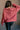 Back view of model wearing the Astro Brick Red Long Sleeve Sweatshirt which features bricked red knit fabric, a raw hem, a ribbed round neckline, dropped shoulders, and long sleeves with raw ruffle details.