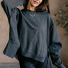 Front view of model wearing the Lyla Washed Black Long Sleeve Sweatshirt which features washed black knit fabric, a ribbed hem with slight slits on each side, raw hem details, a round ribbed neckline, dropped shoulders and long balloon sleeves with ribbed